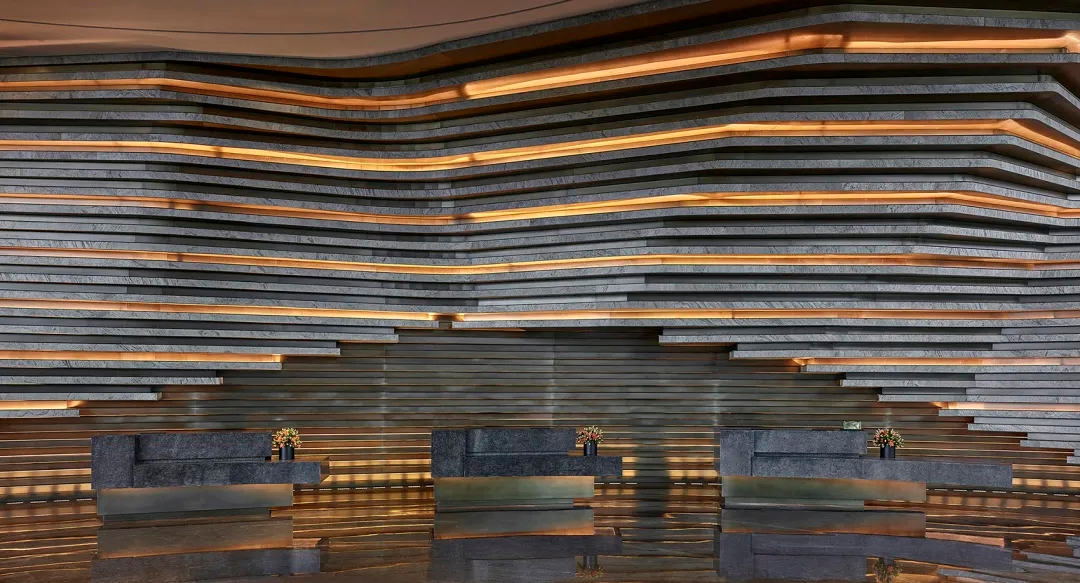 Large hotel interior wall finished with ultra-thin natural stone veneer, layered horizontal surfaces and warm architectural lighting.