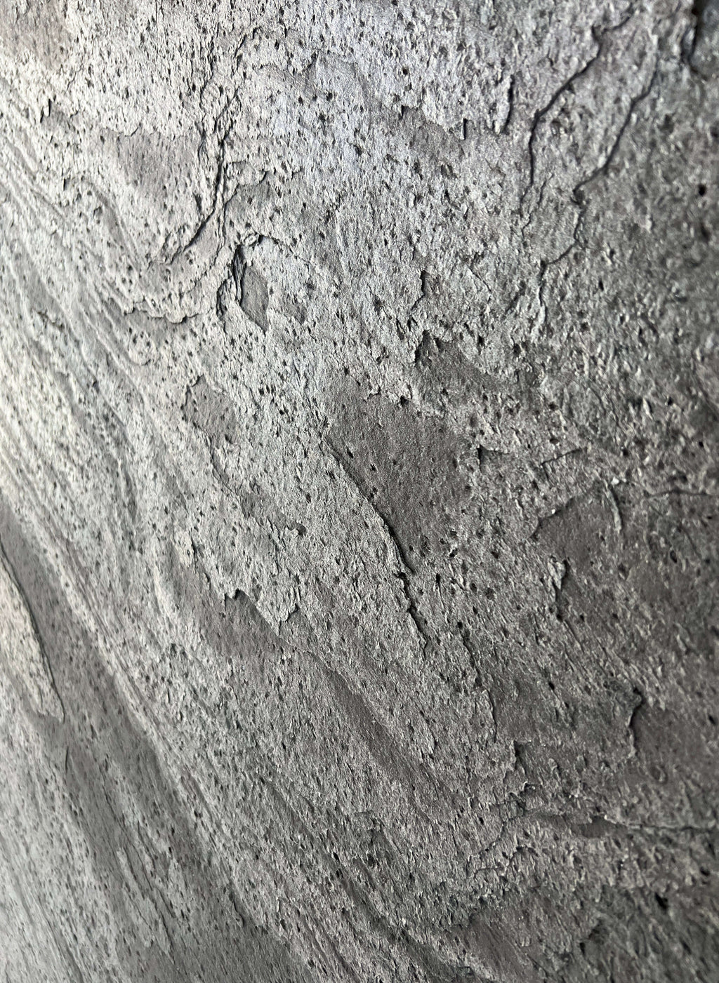 Silver grey natural stone veneer close-up with speckled, pitted stone texture