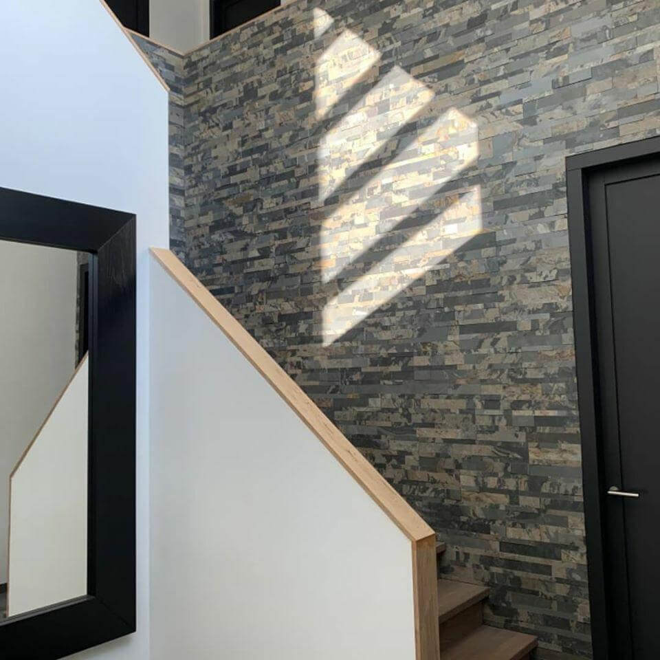 Peel-and-stick stone wall tiles on hallway wall, dark gray and warm tan stacked design.