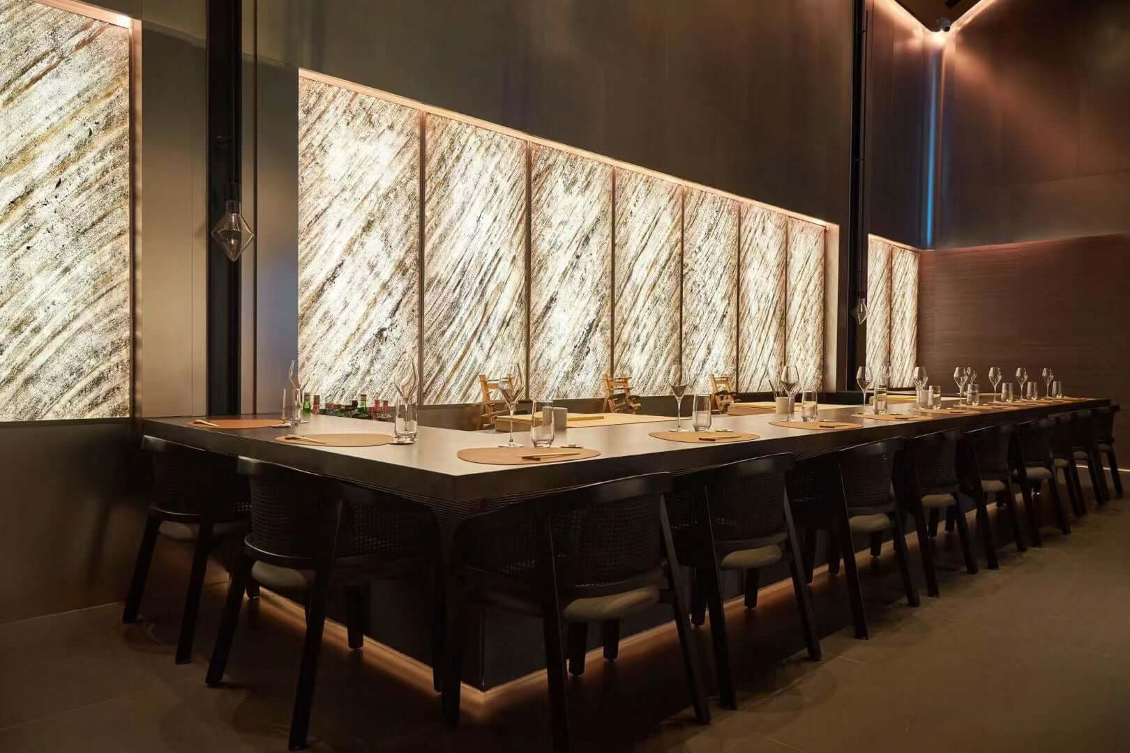 Translucent natural stone wall panels behind dining table in warm lighting