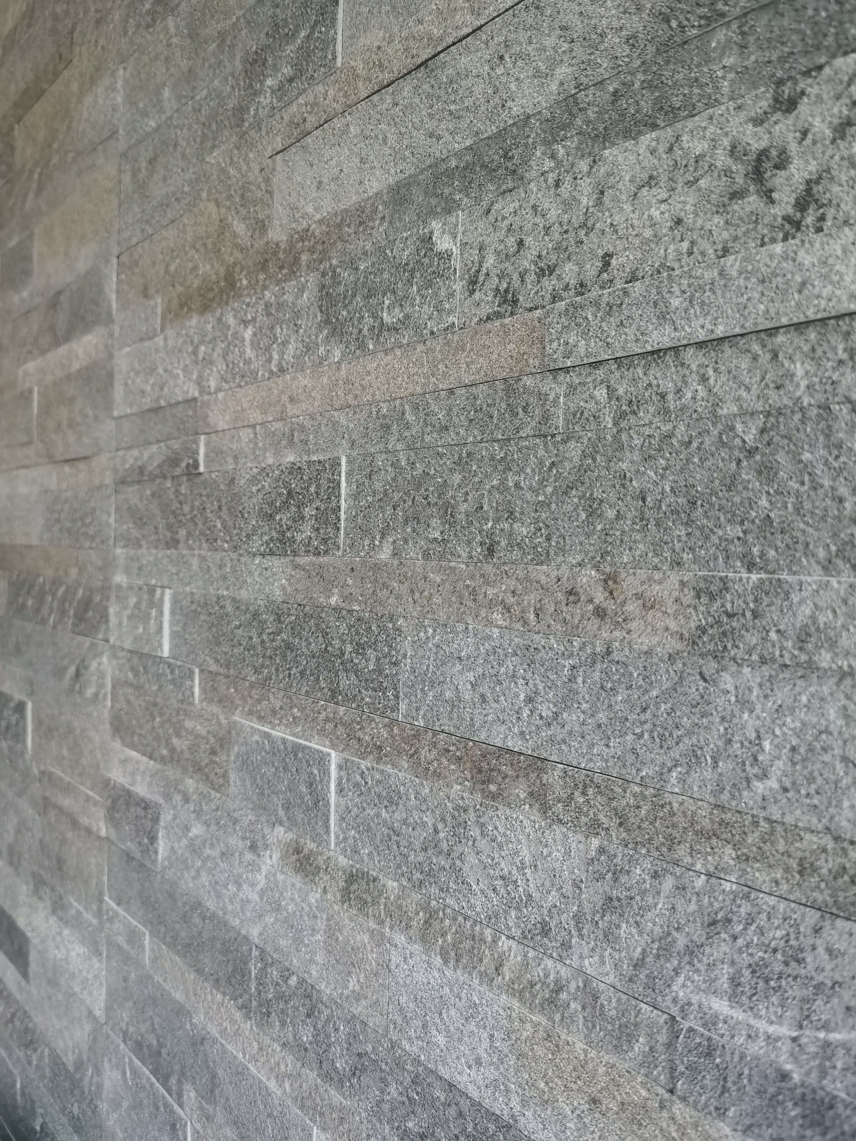 Dark stone tile wall with stacked rectangular texture and visible grout lines