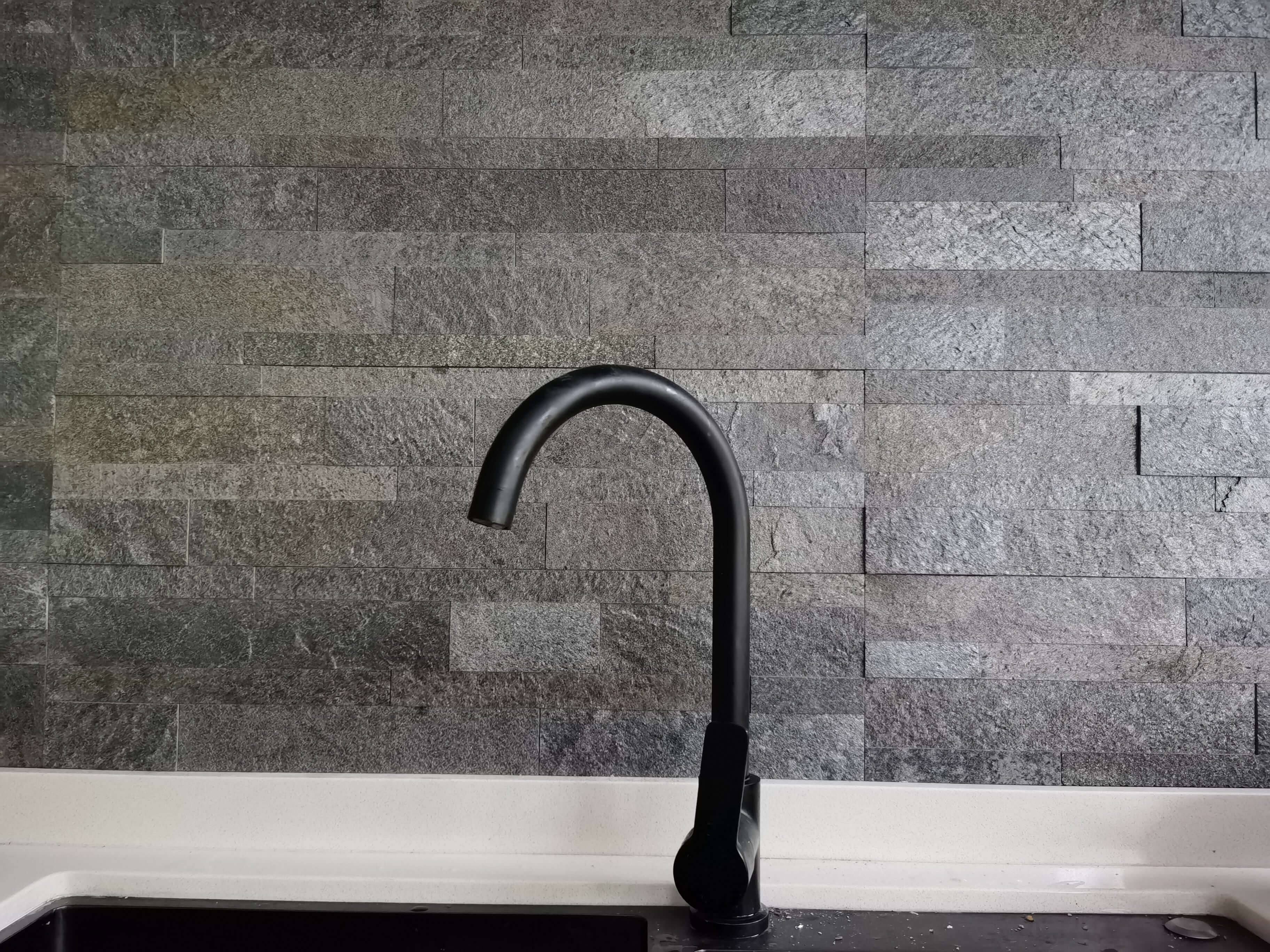 Dark stone tile wall with black curved faucet installed
