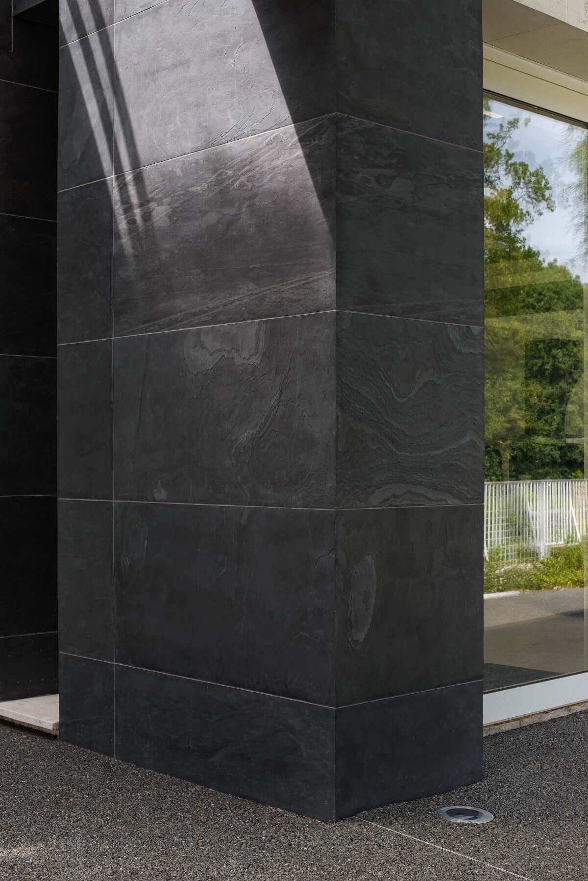 Corner section of black natural stone veneer with dark matte finish and veins